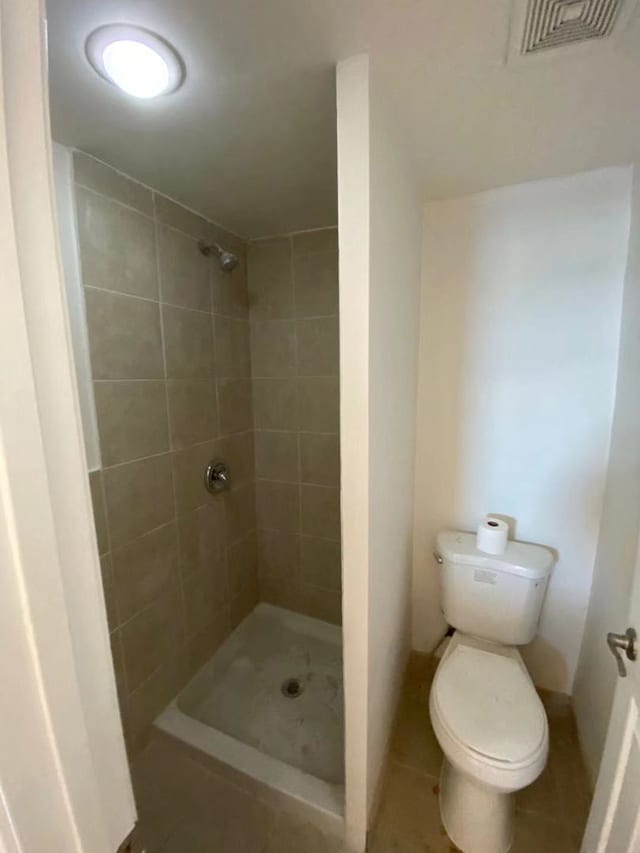 bathroom featuring tile patterned flooring, toilet, and tiled shower