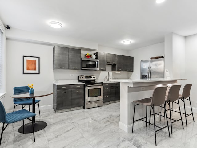 kitchen with appliances with stainless steel finishes, a breakfast bar, sink, kitchen peninsula, and light tile patterned floors