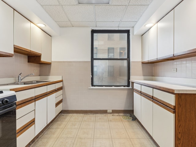 kitchen with white range with electric cooktop, tasteful backsplash, light tile patterned floors, white cabinets, and a paneled ceiling