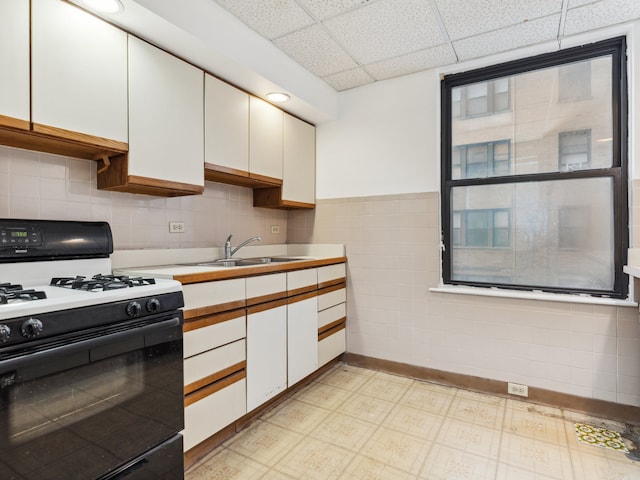 kitchen with light tile patterned flooring, white cabinets, white range with gas stovetop, a paneled ceiling, and sink