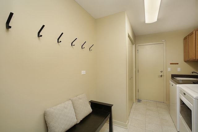 clothes washing area featuring light tile patterned floors, washing machine and dryer, cabinets, and sink