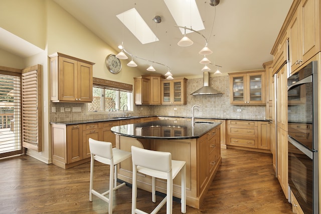 kitchen featuring a skylight, hanging light fixtures, sink, wall chimney exhaust hood, and dark wood-type flooring