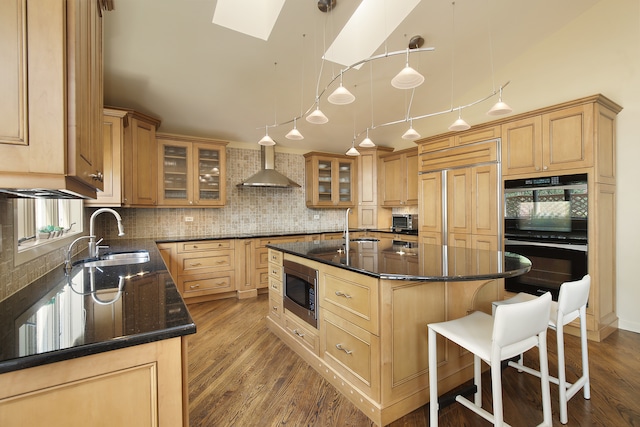 kitchen featuring wall chimney exhaust hood, black appliances, hardwood / wood-style floors, a center island, and sink