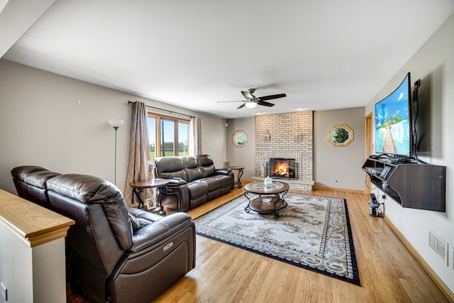 living room featuring brick wall, a fireplace, ceiling fan, and light wood-type flooring