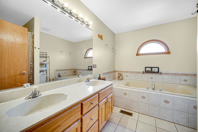 bathroom with tiled tub, dual vanity, and tile patterned flooring