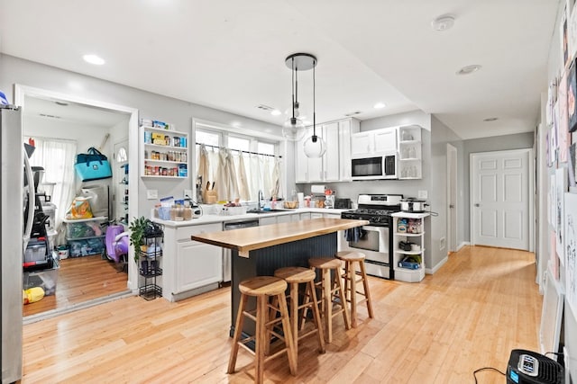 kitchen with light wood-type flooring, appliances with stainless steel finishes, white cabinetry, and a kitchen island