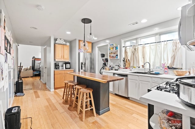 kitchen featuring white cabinetry, stainless steel appliances, a center island, hanging light fixtures, and sink