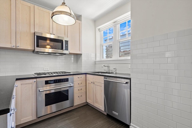 kitchen with stainless steel appliances, tasteful backsplash, light brown cabinetry, hanging light fixtures, and sink