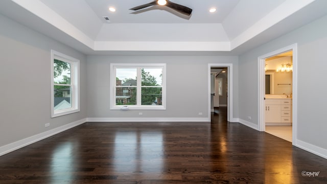 unfurnished bedroom with a raised ceiling, ceiling fan, multiple windows, and dark wood-type flooring