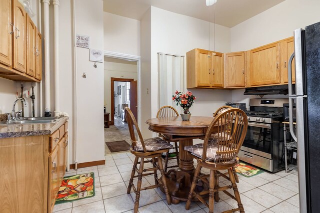 kitchen featuring gas range, light brown cabinetry, sink, light tile patterned floors, and a towering ceiling