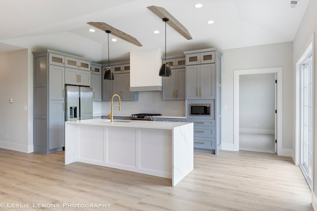 kitchen featuring custom range hood, light wood-type flooring, backsplash, a kitchen island with sink, and stainless steel appliances