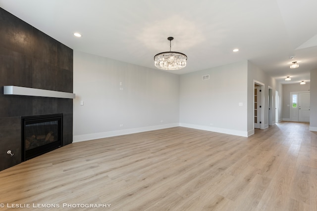 unfurnished living room featuring light wood-type flooring, a large fireplace, and a notable chandelier