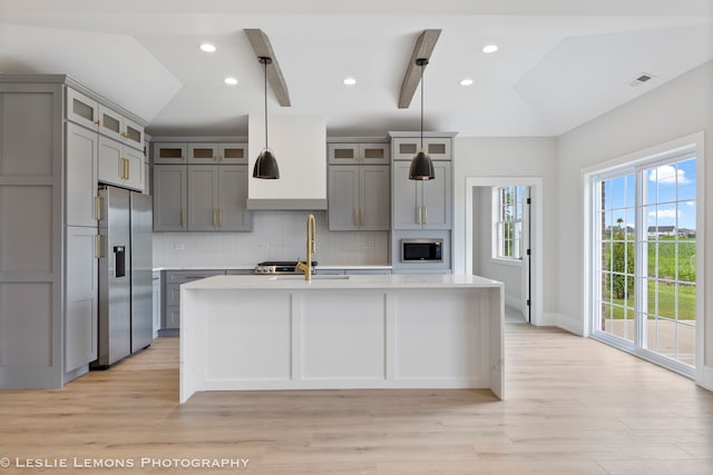 kitchen with vaulted ceiling with beams, tasteful backsplash, light hardwood / wood-style flooring, a kitchen island with sink, and stainless steel appliances