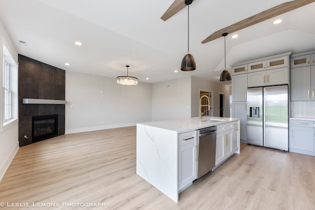 kitchen with appliances with stainless steel finishes, pendant lighting, light wood-type flooring, and a kitchen island with sink