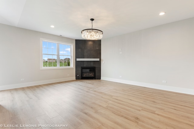 unfurnished living room with a fireplace, light wood-type flooring, and a notable chandelier