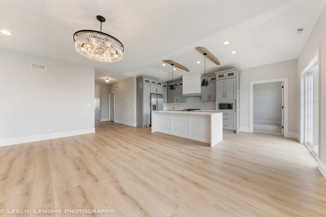 kitchen with decorative light fixtures, an island with sink, lofted ceiling with beams, light hardwood / wood-style floors, and appliances with stainless steel finishes