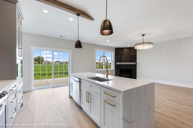 kitchen with sink, hanging light fixtures, light wood-type flooring, light stone countertops, and an island with sink