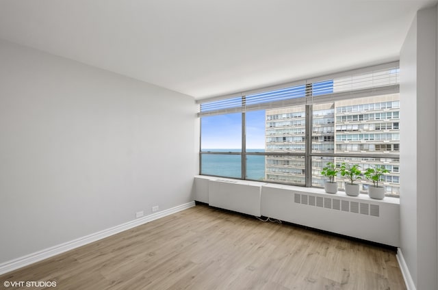 spare room featuring a water view, radiator, and light hardwood / wood-style floors