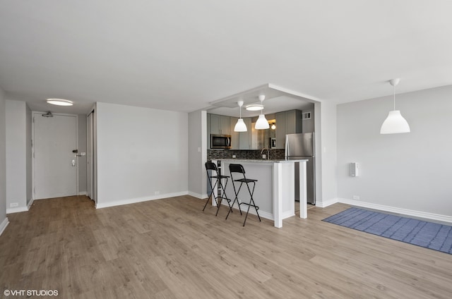 kitchen featuring tasteful backsplash, stainless steel appliances, hardwood / wood-style floors, a kitchen bar, and gray cabinetry