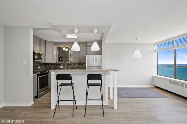 kitchen featuring gray cabinets, stainless steel appliances, light stone counters, light hardwood / wood-style flooring, and backsplash