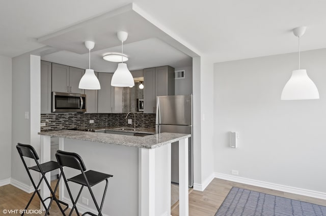 kitchen with light stone countertops, appliances with stainless steel finishes, light hardwood / wood-style flooring, backsplash, and gray cabinetry