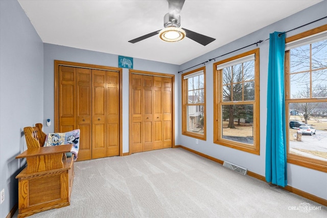 bedroom with a ceiling fan, baseboards, visible vents, multiple closets, and light colored carpet