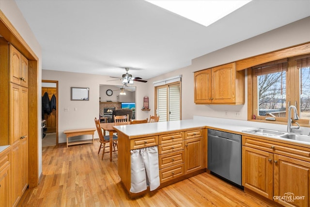 kitchen with a sink, stainless steel dishwasher, a warm lit fireplace, light wood-style floors, and a peninsula