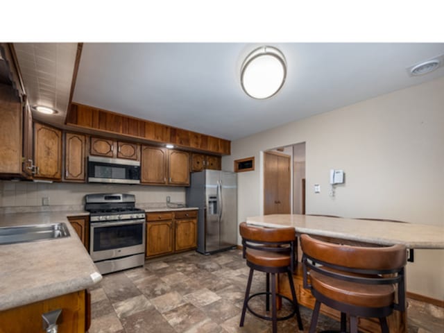 kitchen featuring stone finish floor, brown cabinets, stainless steel appliances, light countertops, and a sink