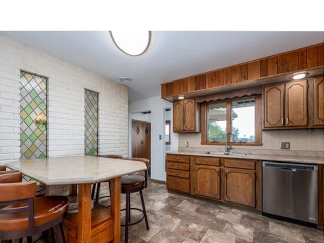 kitchen featuring brown cabinetry, light countertops, a sink, and stainless steel dishwasher