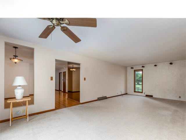 unfurnished room featuring light carpet, ceiling fan with notable chandelier, and baseboards