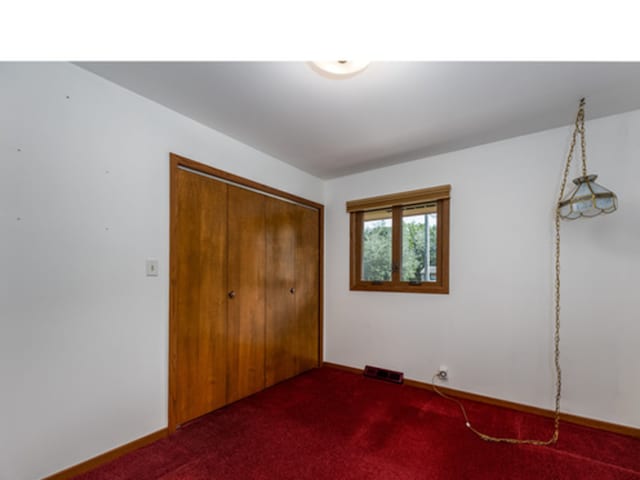 unfurnished bedroom featuring a closet, dark carpet, visible vents, and baseboards