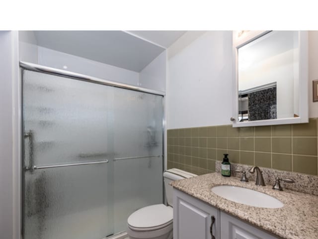 bathroom with toilet, tile walls, a shower stall, and vanity