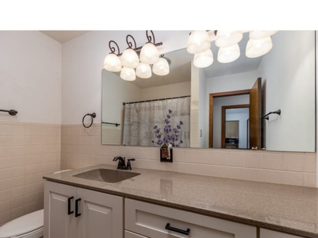 bathroom with toilet, tile walls, and vanity