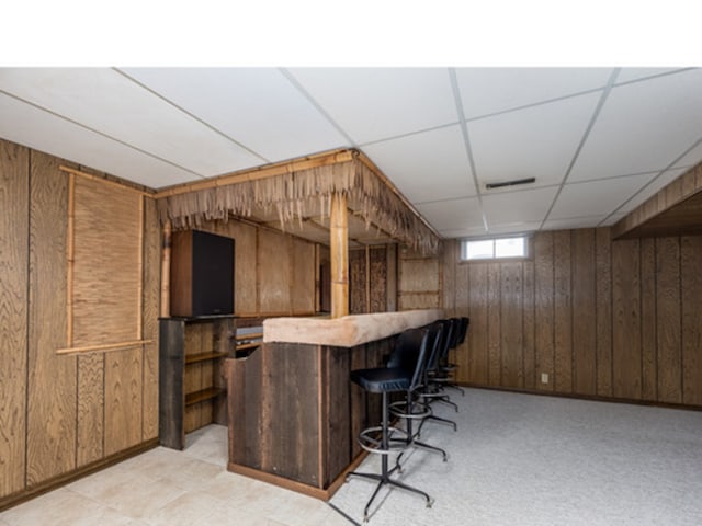 bar with a dry bar, wood walls, and a drop ceiling