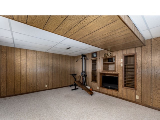 exercise room with a paneled ceiling, wooden walls, a fireplace, and carpet flooring