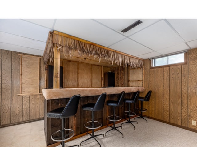 bar featuring a dry bar, wood walls, a drop ceiling, and visible vents