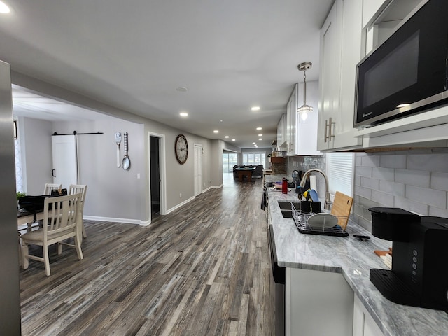 kitchen featuring white cabinetry, tasteful backsplash, dark wood-type flooring, a barn door, and light stone countertops