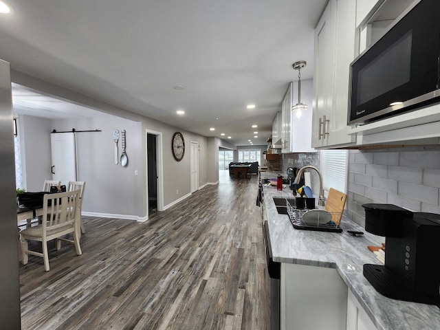 kitchen featuring white cabinetry, black microwave, pendant lighting, and a barn door