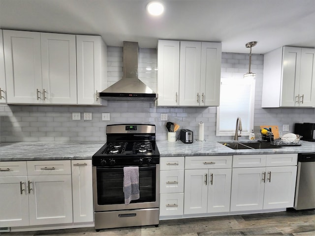 kitchen with hanging light fixtures, stainless steel appliances, wall chimney range hood, white cabinetry, and a sink