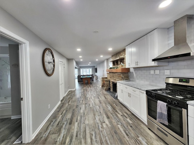 kitchen featuring white cabinets, stainless steel range with gas stovetop, wall chimney range hood, and open shelves