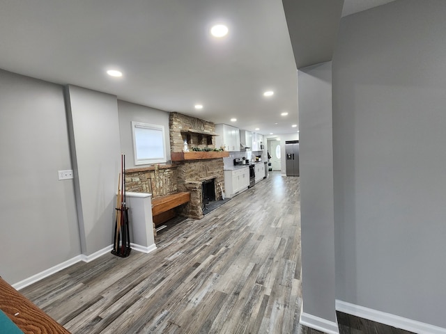 kitchen with a stone fireplace, white cabinetry, hardwood / wood-style flooring, and stainless steel appliances