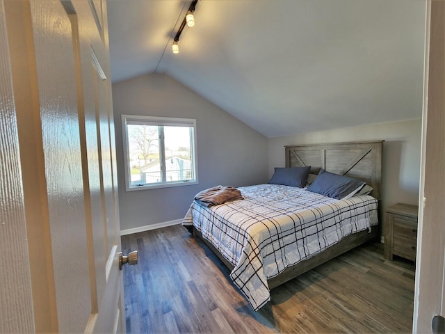 bedroom with dark wood-style floors, rail lighting, vaulted ceiling, and baseboards