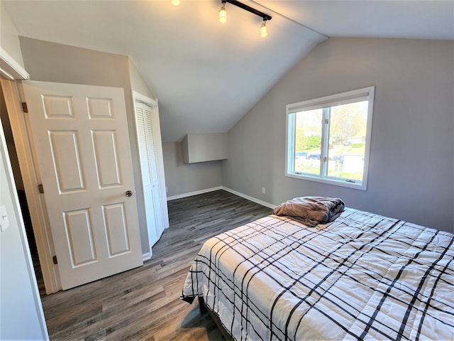 bedroom featuring lofted ceiling, rail lighting, a closet, and hardwood / wood-style flooring