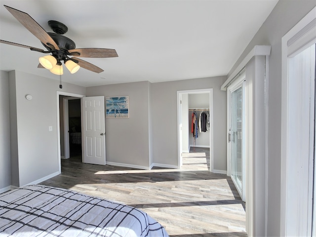 unfurnished bedroom featuring a spacious closet, wood-type flooring, a closet, and ceiling fan