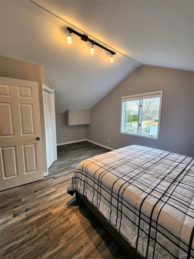 bedroom featuring vaulted ceiling, track lighting, dark wood-style flooring, and baseboards