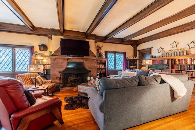 living room with a brick fireplace, beam ceiling, and light wood-type flooring