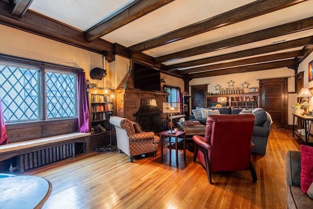 living room featuring radiator heating unit, beamed ceiling, a brick fireplace, and hardwood / wood-style floors