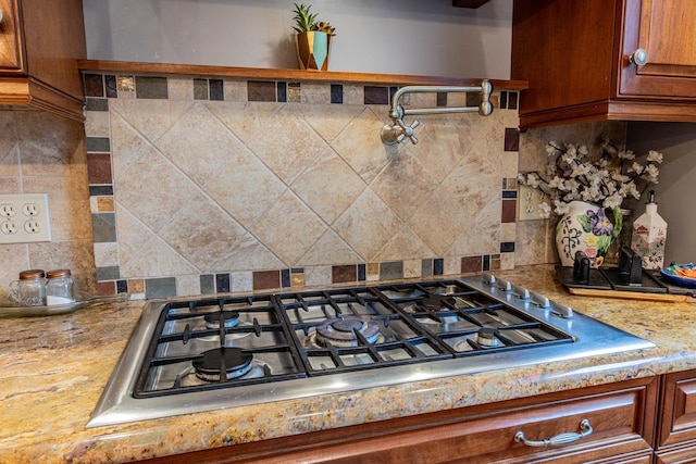 room details with light stone counters, decorative backsplash, and stainless steel gas cooktop