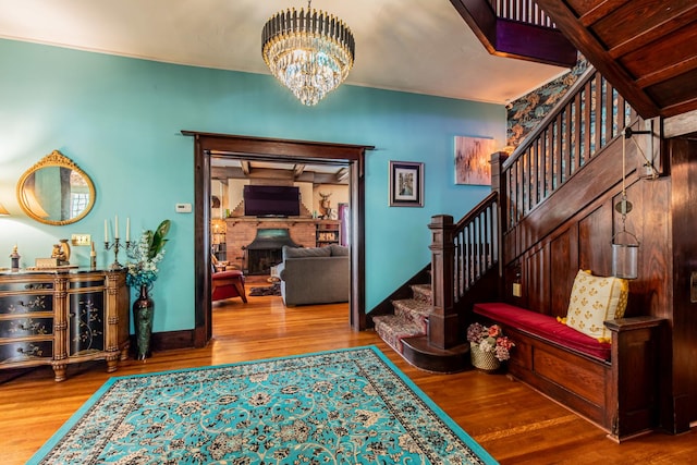 entrance foyer featuring wood-type flooring, a stone fireplace, and an inviting chandelier