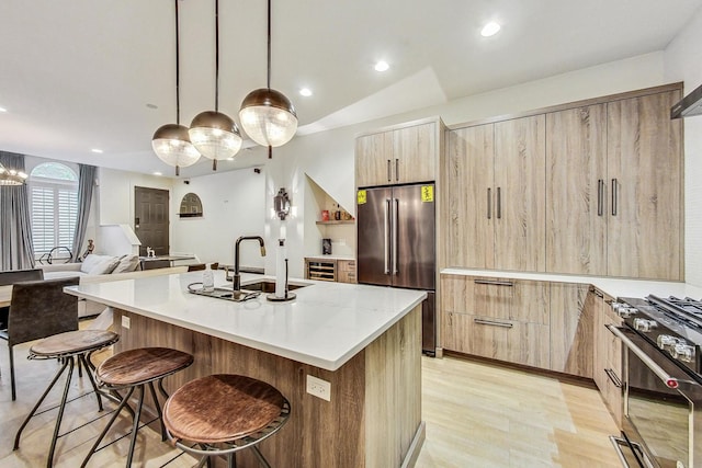 kitchen with pendant lighting, a kitchen island with sink, sink, light hardwood / wood-style flooring, and high quality fridge